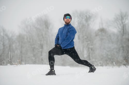Preview: Male athlete in blue jacket and black leggings performs a lunge exercise in a snowy landscape with t