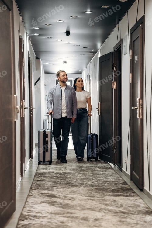 Preview: Couple walking down a hotel corridor with luggage, modern decor, and doors visible on both sides, sh