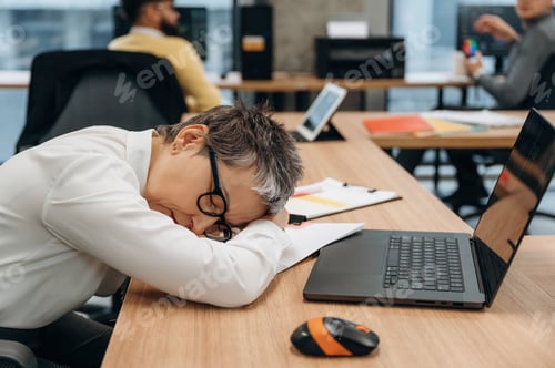 Preview: Businesswoman resting her head on desk in modern office environment, showcasing fatigue and the chal