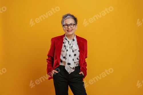 Preview: Stylish older woman with short gray hair wearing a red blazer and polka dot blouse, smiling confiden