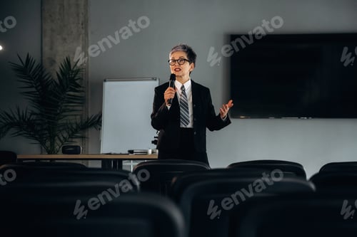 Preview: Business professional in black suit delivers presentation with microphone in modern office setting,