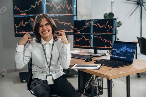 Preview: Young man is sitting in the office with multiple displays of stock market data