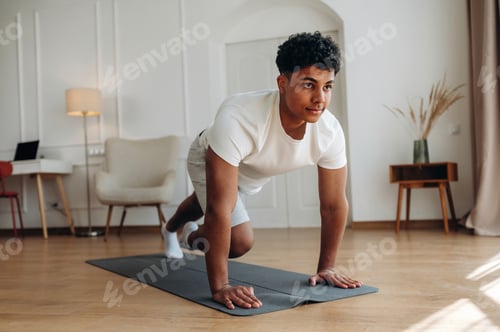 Preview: Young male exercising on a yoga mat in a bright indoor space, wearing a white t-shirt and shorts, wi