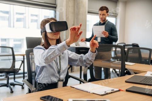 Preview: Woman wearing virtual reality headset interacts with digital interface while man holds documents in