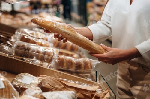 Preview: Individual is selecting a fresh baguette from a bakery display, surrounded by various types of bread
