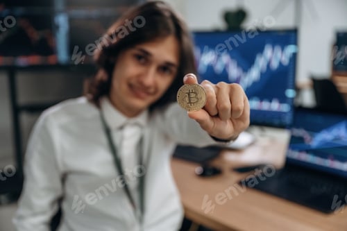 Preview: Golden colored crypto coin. Young man is sitting in the office with multiple displays of stock marke