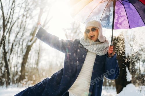 Preview: Young woman in winter attire joyfully poses with a colorful umbrella while snowflakes fall around he