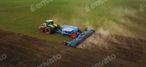 Preview: Agricultural tractor with blue seed drill working on a large field, creating dust clouds while prepa