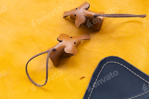 Preview: Two Handmade Leather Bear Keychains with Cord on Yellow Leather Surface Next to Navy Wallet