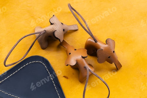Preview: Two Handmade Leather Bear Keychains with Cord on Yellow Leather Surface Next to Navy Wallet