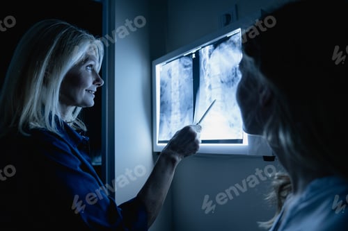 Preview: Woman doctor showing X-ray results to female patient in medical office, in the dark