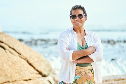 Preview: Arms crossed, smile and portrait of old woman at beach for summer vacation, retirement and relax