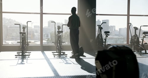 Preview: Back, fitness and man thinking by gym window for reflection, wellness or view with stationary bike