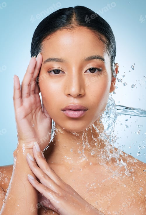 Preview: Woman, water splash or portrait with skincare in studio for face wash on a blue background