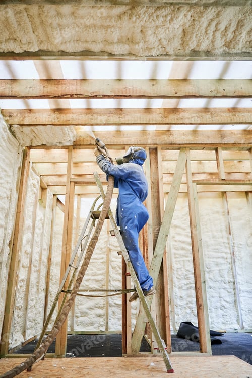 Preview: Worker spraying polyurethane foam insulation under roof beams in timber frame house
