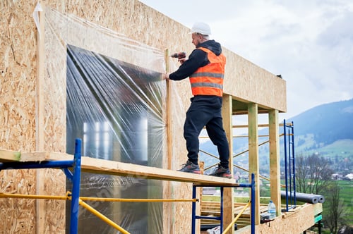 Preview: Construction worker on scaffold fixing vapor barrier film over OSB wall with drill