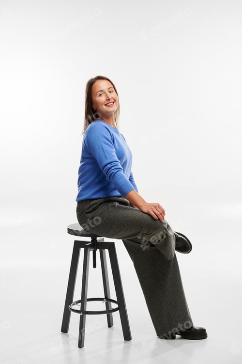 Preview: Woman sitting on stool and smiling at camera in studio. Young adult Caucasian