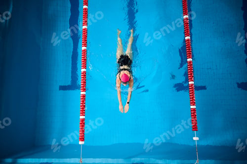 Preview: Female swimmer gliding underwater in pool, wearing pink cap and swimsuit