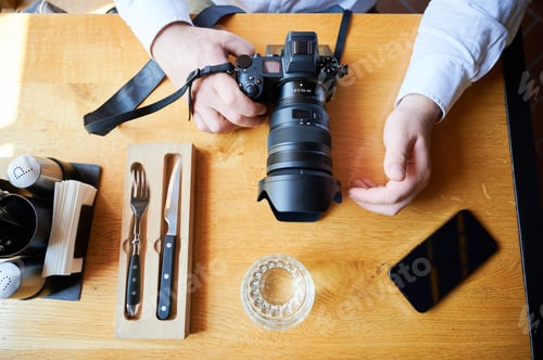 Preview: Top view of photographer hands holding camera on cafe table, adjusting lens before shooting