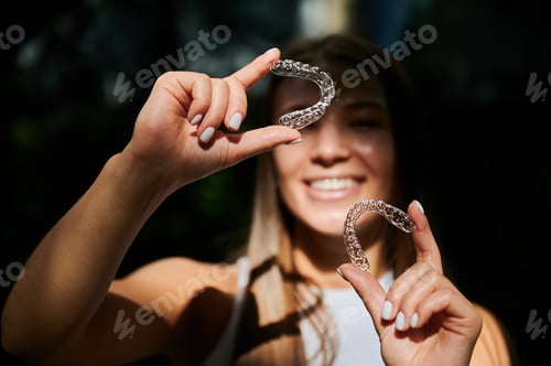 Preview: Smiling woman demonstrates transparent aligners in sunlit close up