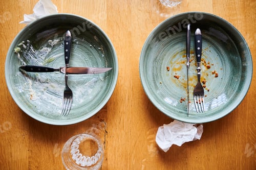 Preview: Two empty plates with cutlery after meal on wooden table, leftovers and crumbs visible