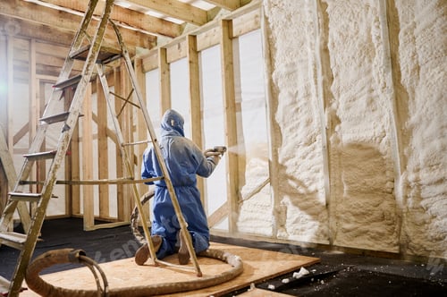 Preview: Worker kneeling and spraying polyurethane foam insulation into wall cavity of timber frame house