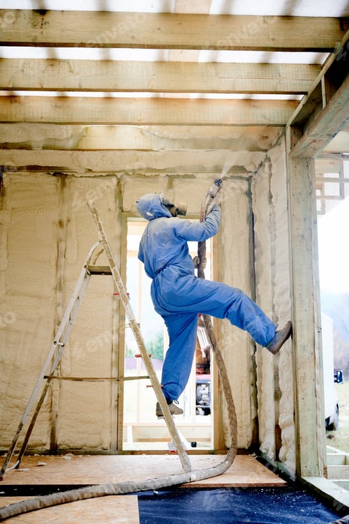 Preview: Worker spraying polyurethane foam insulation on upper wall and ceiling corner in timber frame house