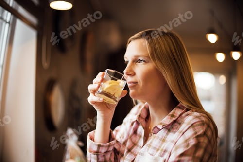 Preview: Caucasian woman in plaid shirt holding a glass with ice and lemon slice, gazing thoughtfully out of