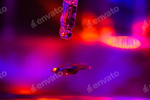 Preview: Close-up of a dropper releasing a droplet of liquid against a vibrant, colorful background with purp