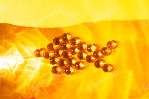 Preview: Group of amber-colored gel capsules arranged in an arrow shape on a bright yellow background, showca