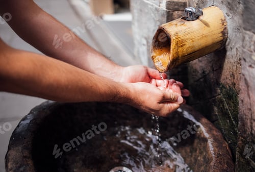 Preview: Hands of a person washing under a bamboo water spout, with a stone basin filled with water, showcasi