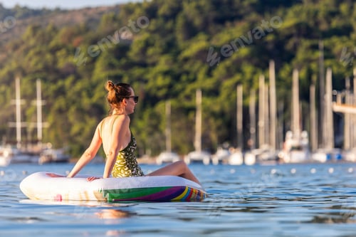 Preview: Woman wear green swimsuit relax inflatable ring calm sea near yachts forested coast sunset warm summ