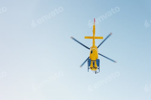 Preview: Scenic bottom view modern yellow rescue emergency mountain helicopter flying against clear blue sky.