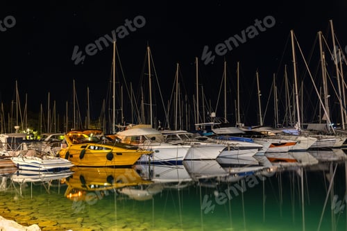 Preview: Night marina pier between moored yachts under dark starry sky navigation lights reflecting calm wate