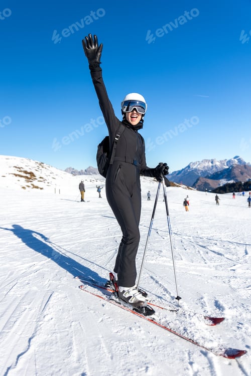 Preview: Portrait young adult happy smiling woman skier wear black outfit overall stand snowy slope raised wa
