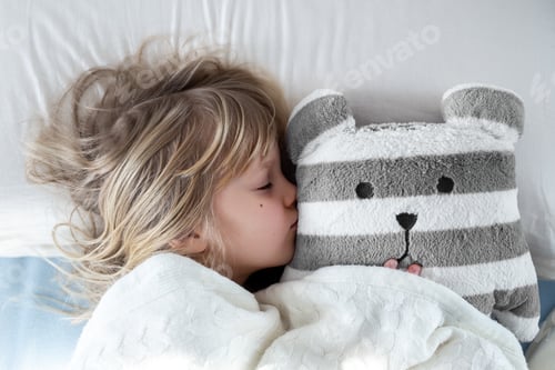 Preview: Cute child sleeping on bed hugging plush toy close to face seeking comfort safety bright bedroom in