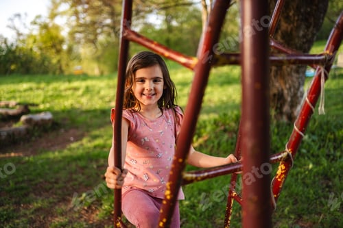 Preview: Smiling girl climbing a colorful playground structure in spring