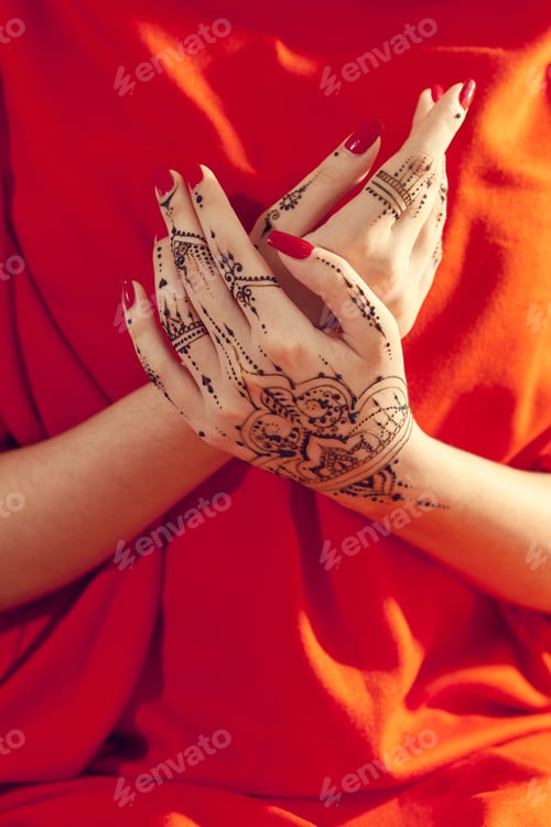 Preview: Hands with henna designs resting together on a red fabric surface