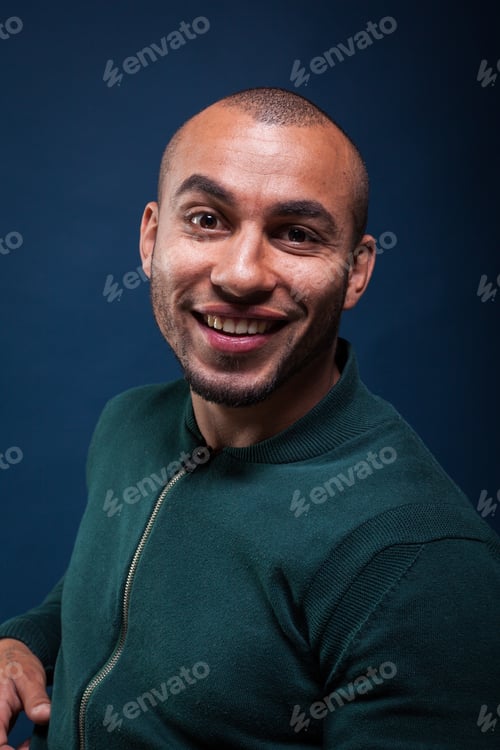 Preview: Smiling man in green sweater poses against dark blue background indoors