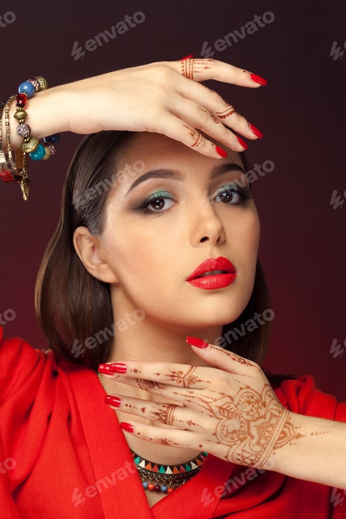 Preview: Model showcases red lips and henna designs with hands raised in front of face