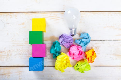 Preview: Colorful blocks and crumpled paper next to a light bulb on a wooden surface