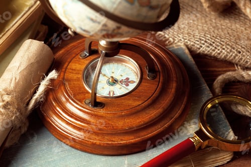 Preview: Old compass sits on wooden table next to globe and magnifying glass in a study room