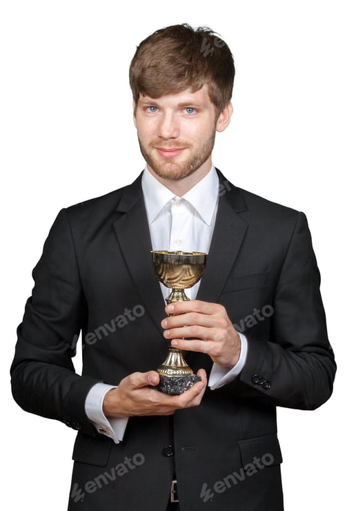 Preview: Man in suit holds trophy at indoor event after winning a competition in the evening