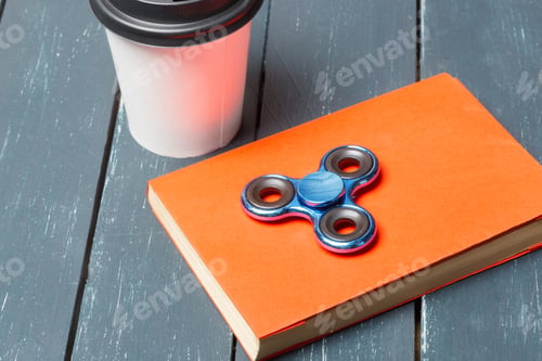 Preview: Fidget spinner rests on an orange notebook beside a coffee cup on a wooden table
