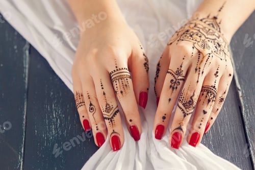 Preview: Hands with henna designs resting on a cloth with red nails painted