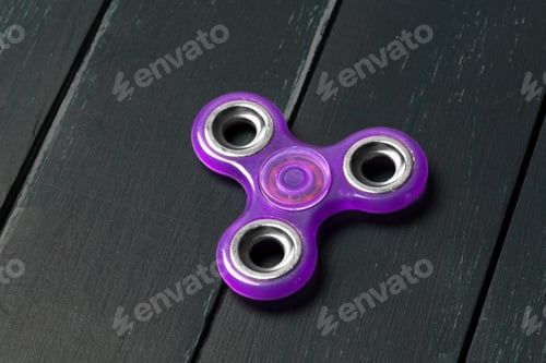 Preview: Toy fidget spinner rests on black wooden table surface in a home setting