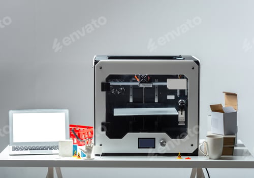 Preview: 3D printer sits on white table with laptop and other items in a work space