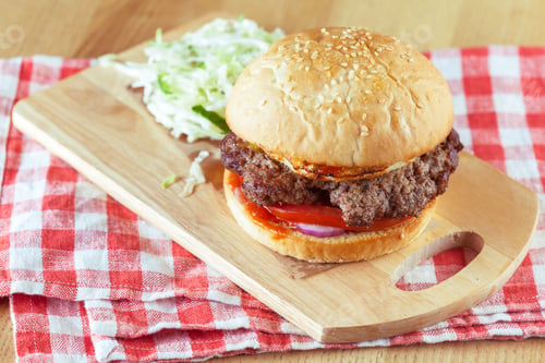 Preview: Delicious burger served on a wooden board with fresh vegetables at a casual setting