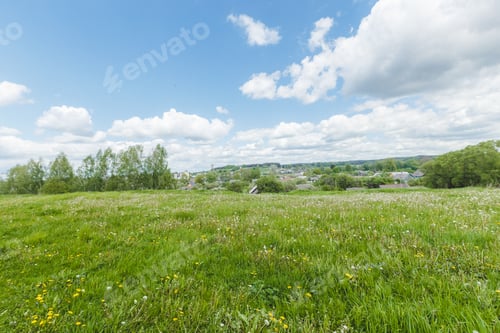 Preview: Wide view of grassland with clouds and distant trees in a bright sky