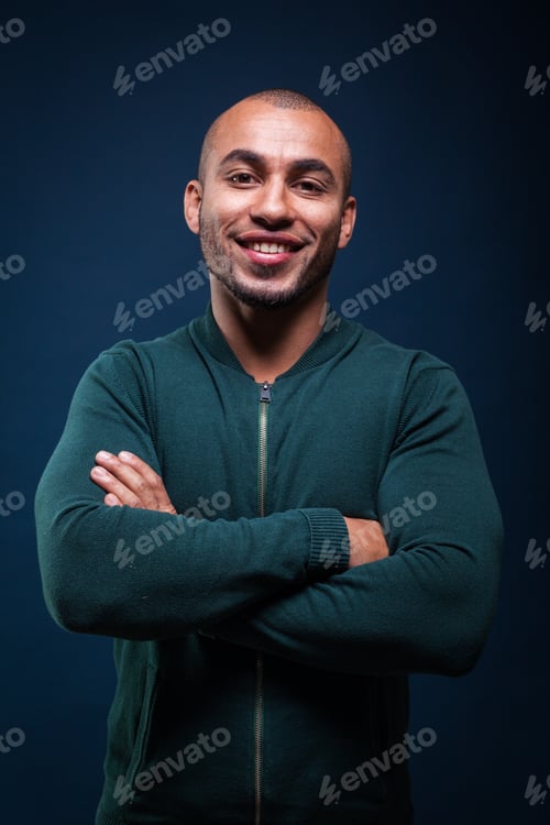 Preview: Smiling man stands with crossed arms in a dark blue background